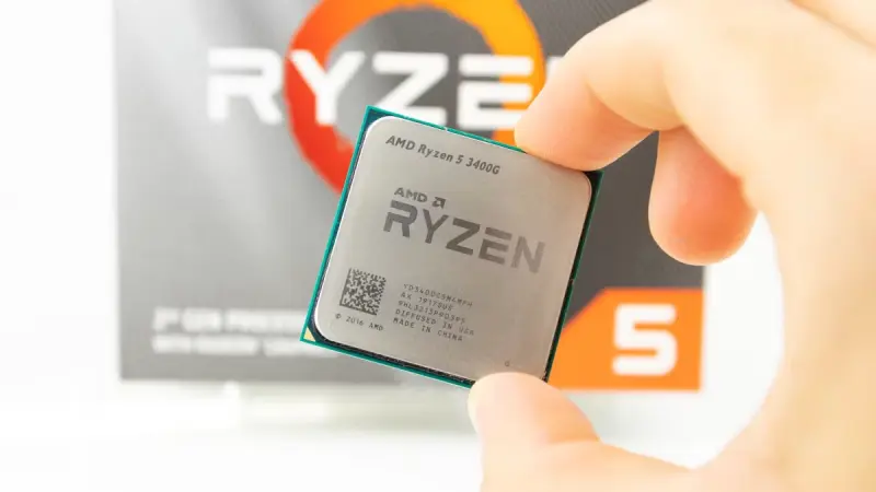 Κοντινό πλάνο μιας CPU AMD Ryzen 5 3400G που κρατείται ανάμεσα στα δάχτυλα ενός ατόμου